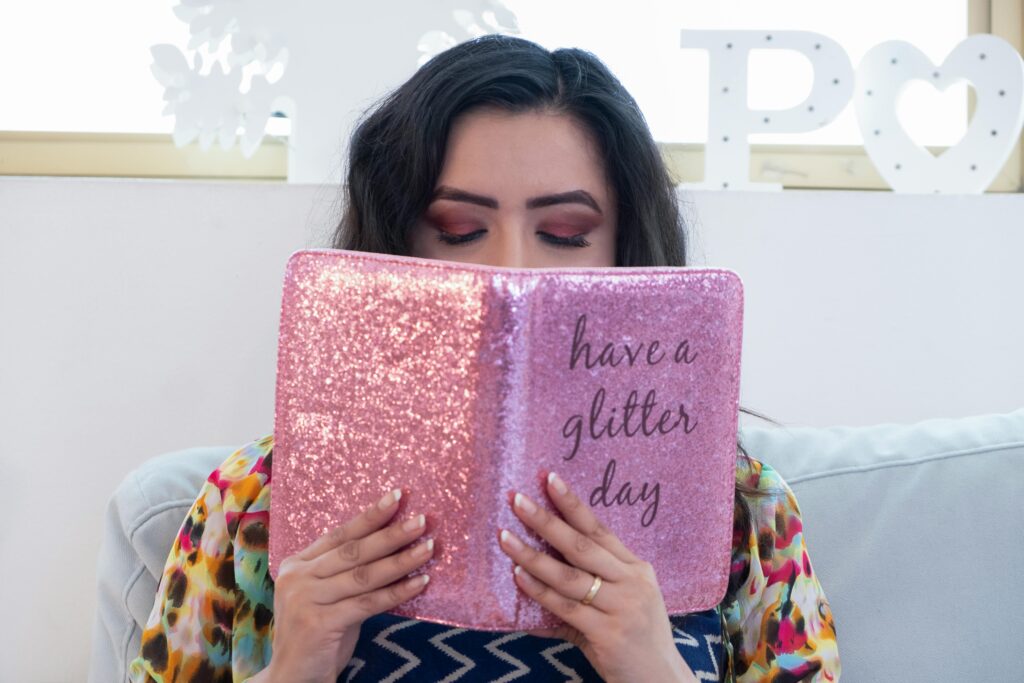 A young woman enjoys leisure time indoors with a sparkly pink journal promoting positivity.